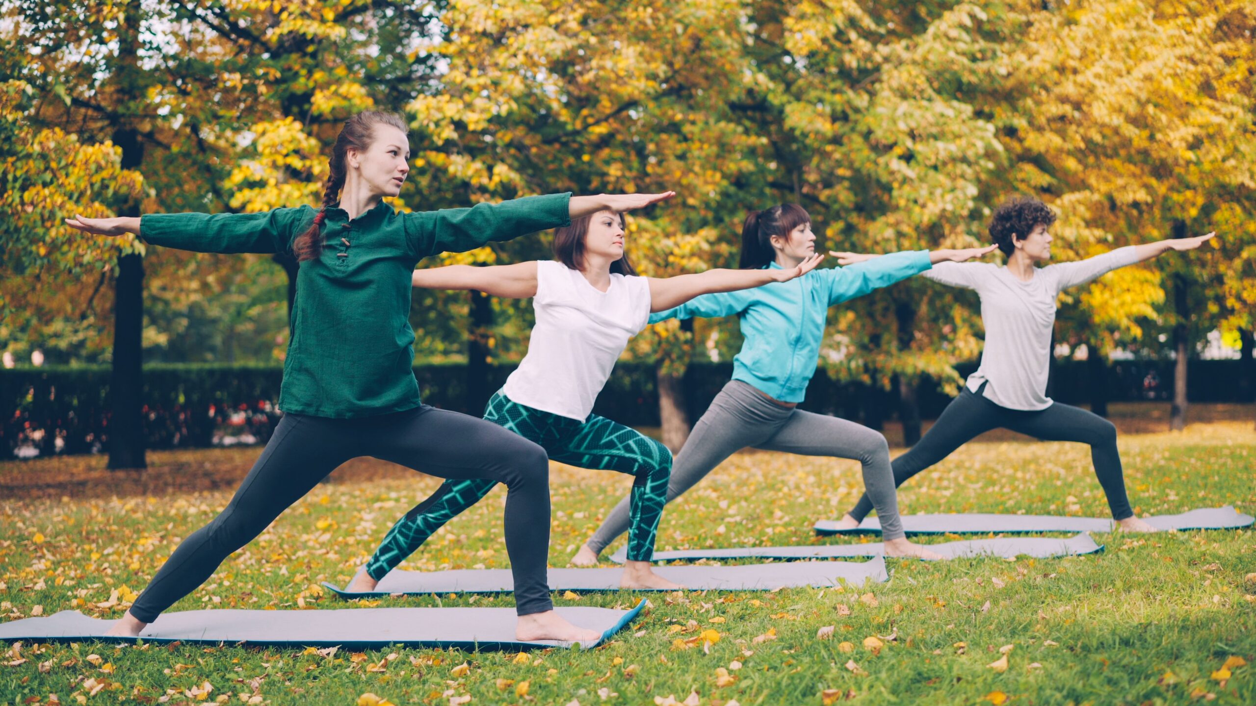 Group of people practicing yoga poses outdoors in a park as part of a weekly wellness routine.