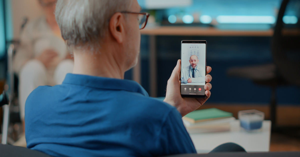 Older man using smartphone for telehealth consultation with doctor via video call.