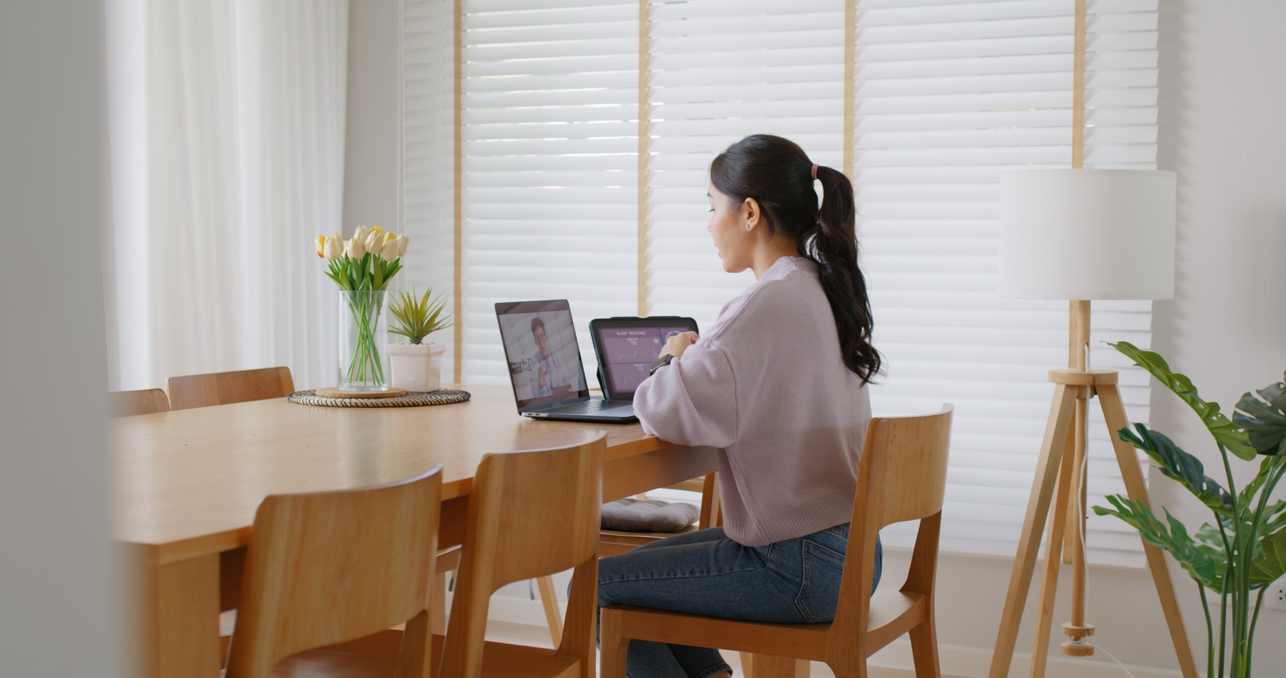Woman attending an online consultation on a laptop at a bright home dining table.